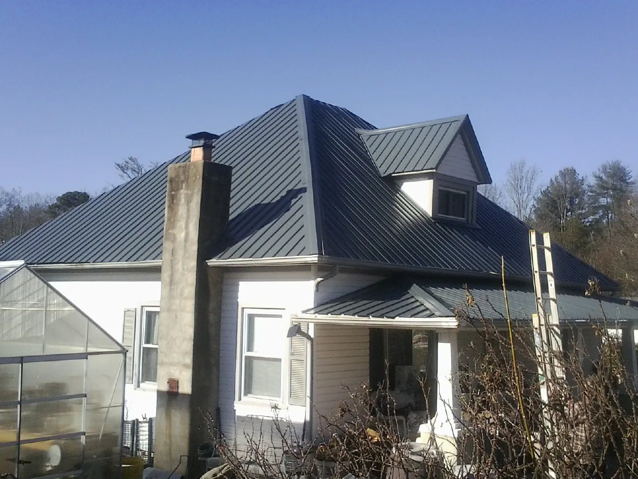 Dark blue standing seam metal roof on a white farmhouse with dormer — Slate & Tile Roof Repair by Roofing Brothers in Mackey