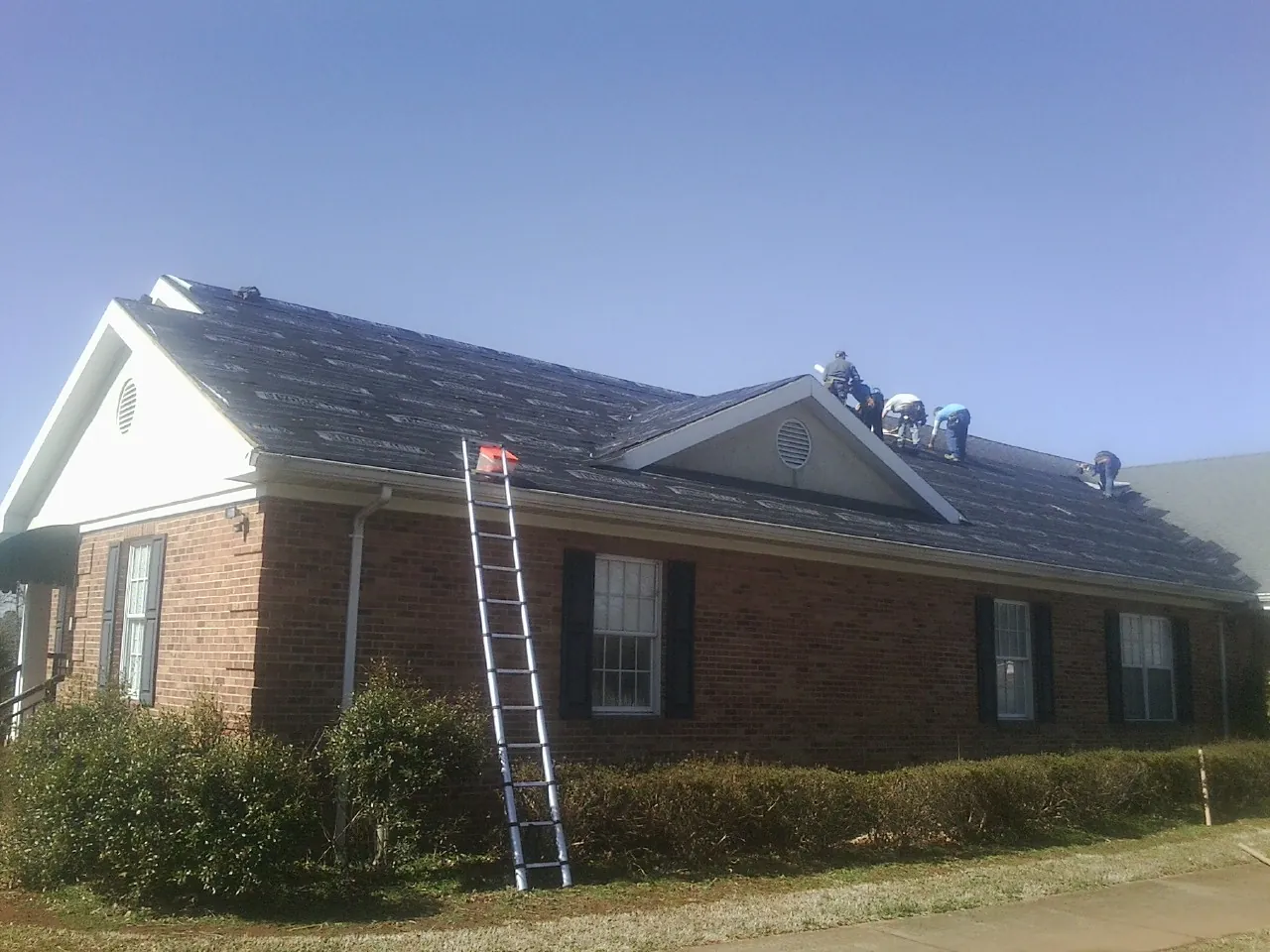 Crew tearing shingles off a brick ranch roof with a ladder set — Emergency Roof Repair work by our crew in Mackey