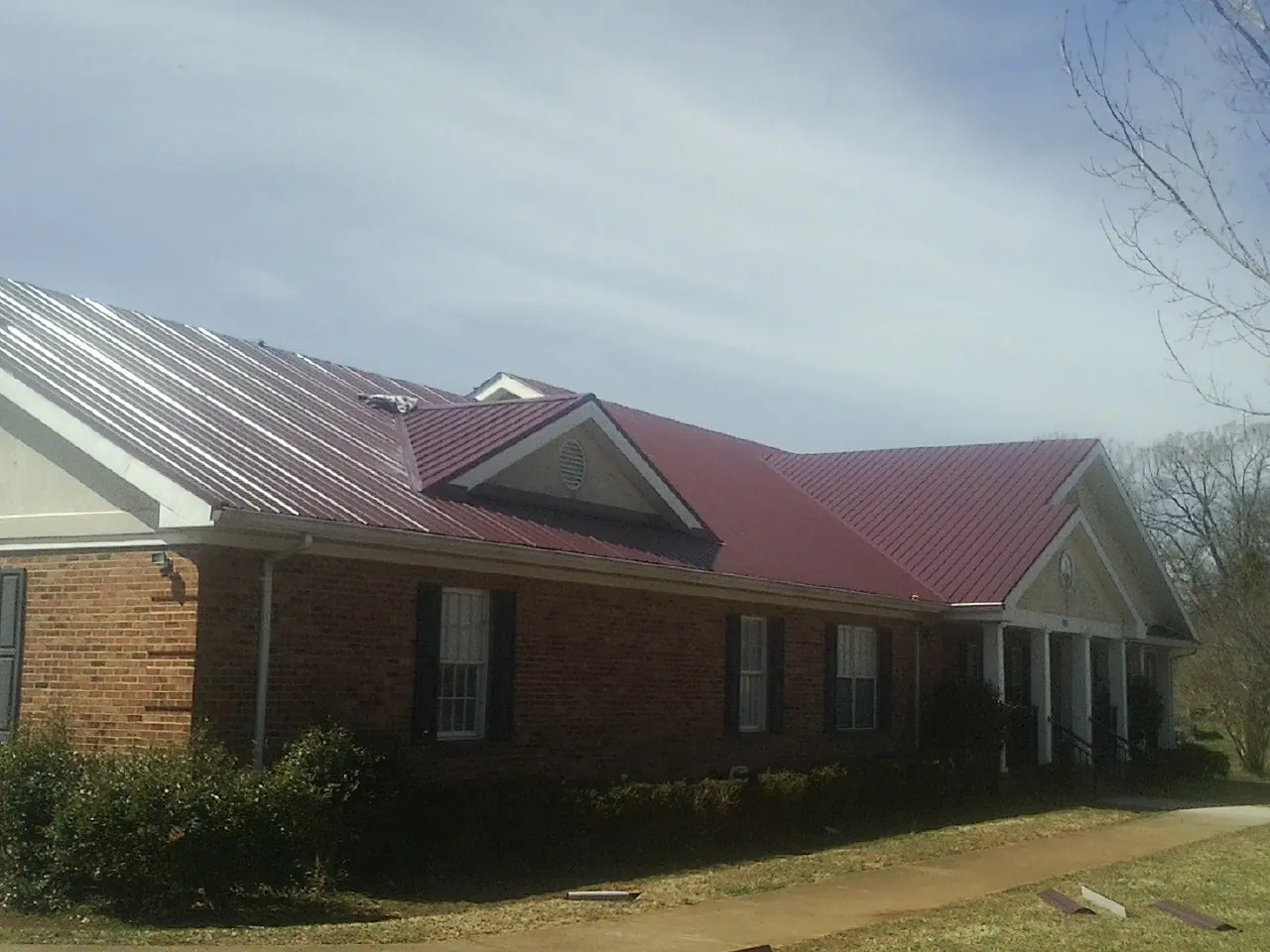 Red metal roof with gabled entries on a long brick building, from a Hail Damage Roof Repair job in Mackey