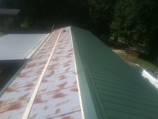 Old rusted panels beside newly installed green metal roofing — Wind Damage Roof Repair by Roofing Brothers in Mackey