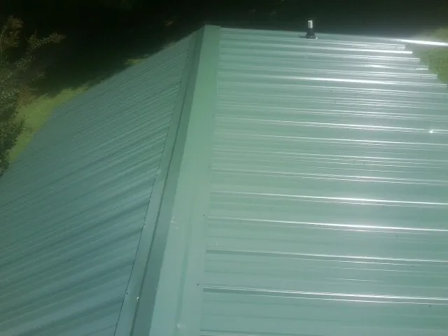 New green metal panels meeting at the ridge of a roof — Flat Roof Repair work by our crew in Mackey