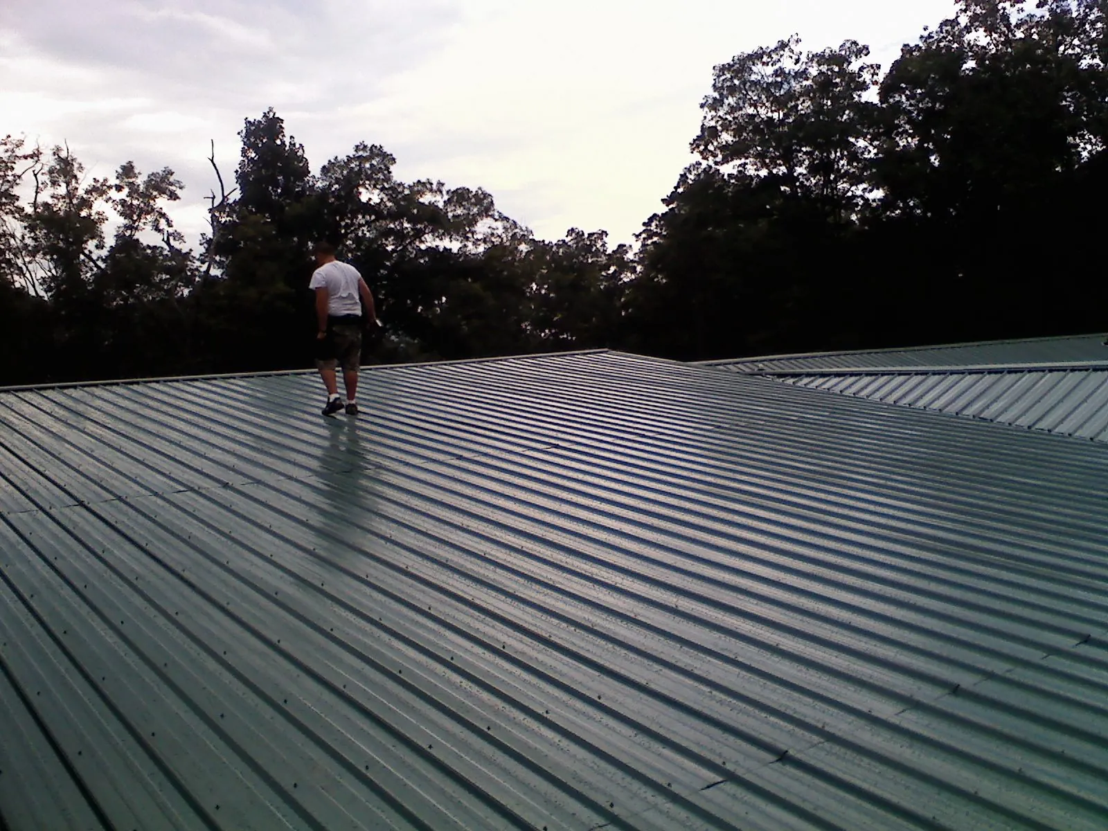 Roofer walking a wide expanse of new green metal roofing in Mackey