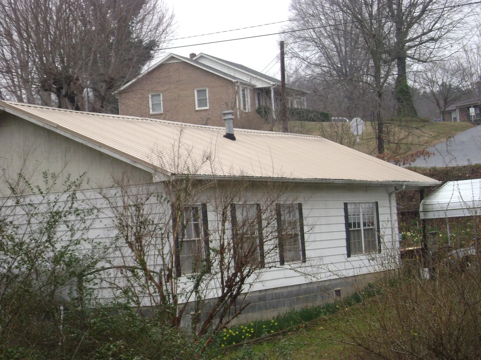 Tan metal roof on a white sided house set into a hillside — Commercial Roofing by Roofing Brothers in Mackey