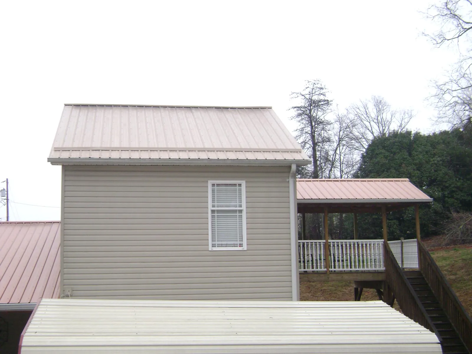 Tan metal roofs on a two story addition and attached porch, from a Roof Replacement job in Mackey